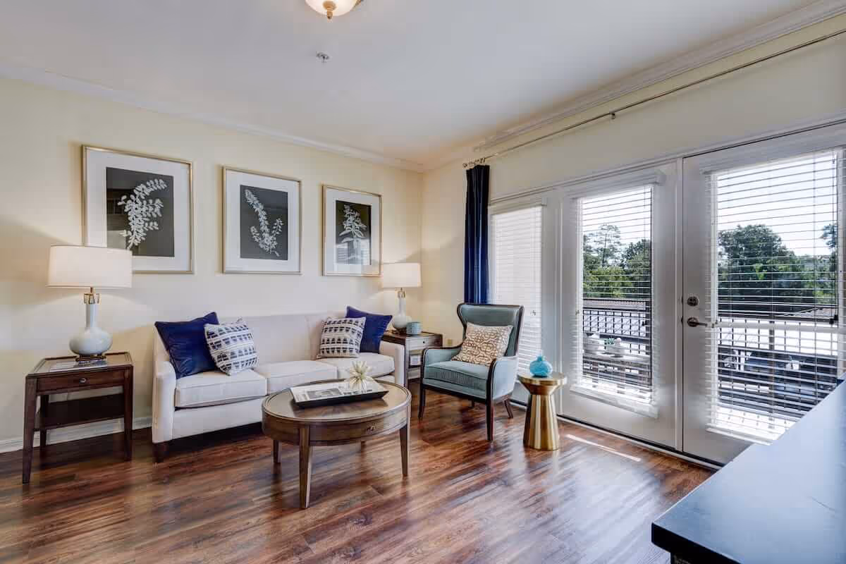 Bright living room with a sofa, armchair, coffee table, side tables and large glass doors opening to a balcony.