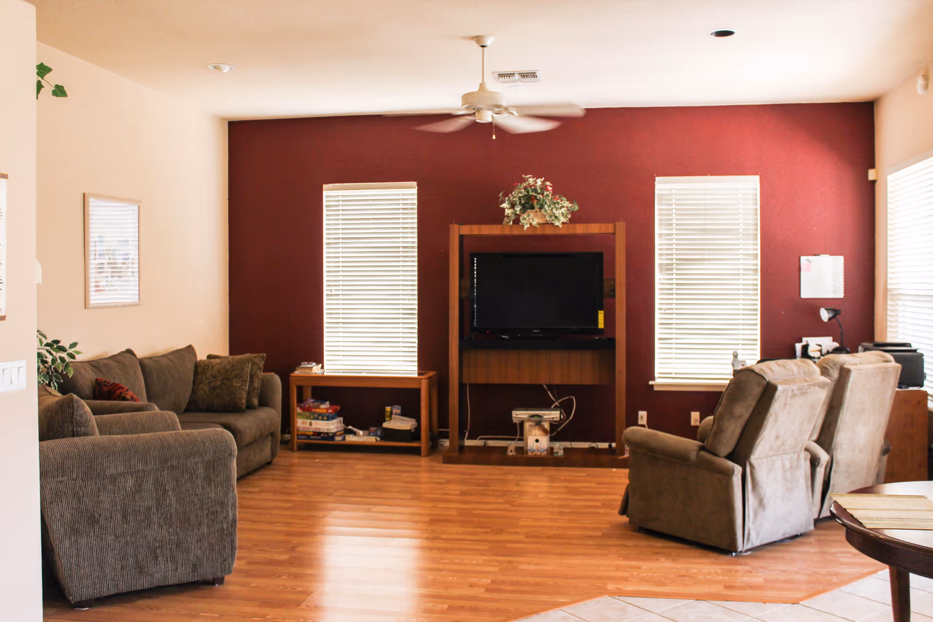 Spacious living room with sofas and recliners facing a TV on a wooden stand against a red accent wall and hardwood floors.