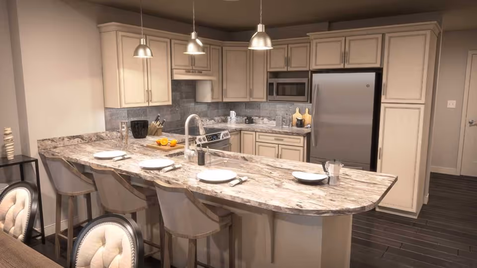 Modern kitchen with beige cabinetry, stainless steel refrigerator, microwave, and stove. A marble countertop island with four bar stools is set with plates and napkins. Three pendant lights hang above the island.