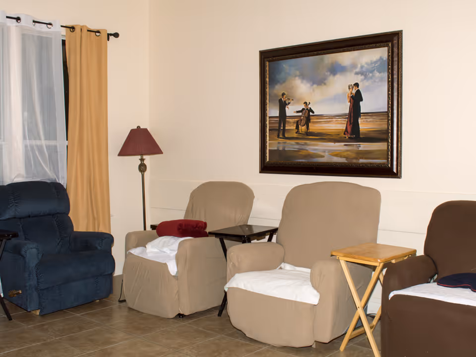 A sitting area with upholstered recliners, small side tables, a floor lamp, and framed artwork on the wall.