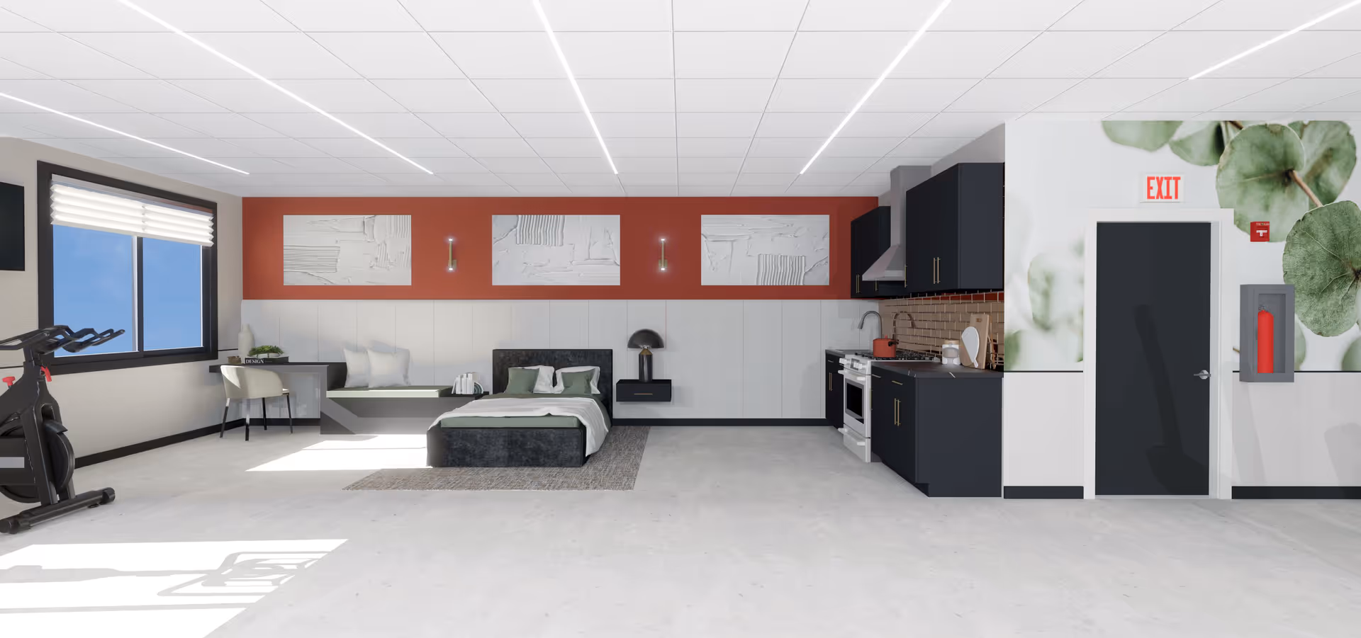 A spacious, modern room featuring a bed with pillows and a blanket, a small desk with a chair near a window, a stationary exercise bike, and a kitchenette with black cabinets, a stove, and a sink. The walls are decorated with three abstract art pieces above the bed and a large leafy plant mural near an exit door. The floor is light-colored and the ceiling has recessed lighting.