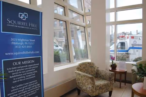 Lobby area with patterned armchairs, a Squirrel Hill banner, and large windows.