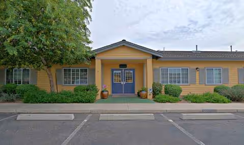 Front view of a memory care facility entrance, yellow exterior with blue doors.