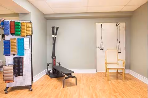 Therapy room with bench, resistance bands, and a suspended chair in a light rehab space