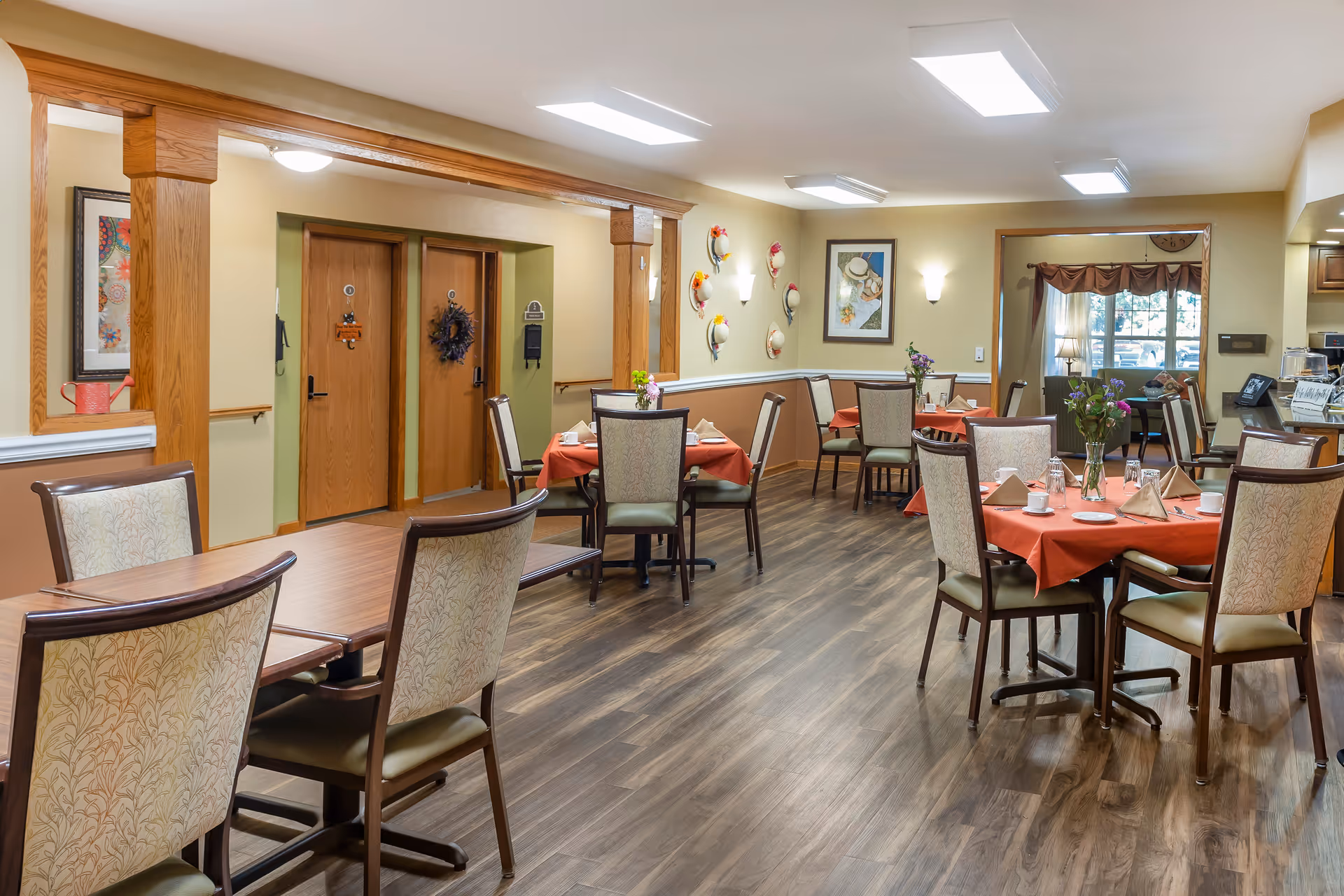 Bright dining room with multiple set tables and chairs, wood flooring, and decorative wall accents.