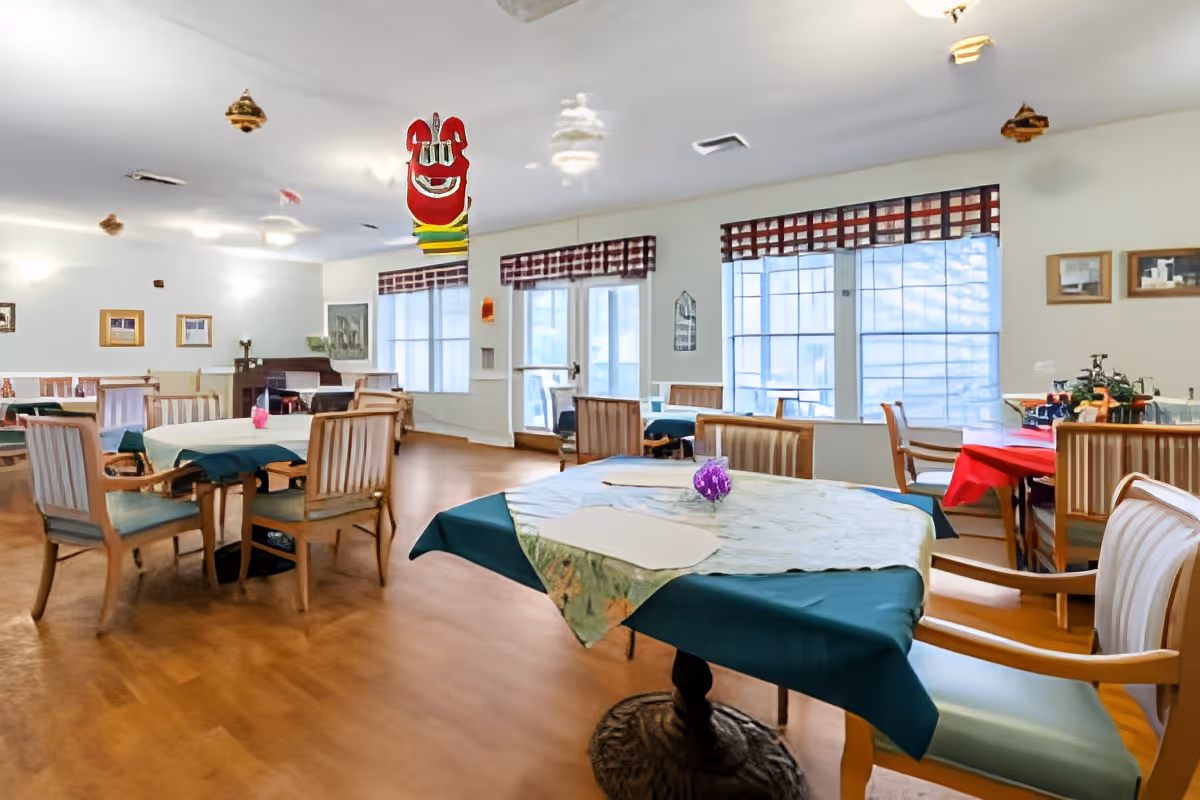 Spacious dining room with several tables and chairs, large windows with valances, and hanging decorations from the ceiling.