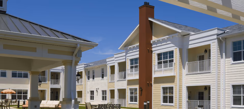 Sunny exterior courtyard of a beige and white two-story senior living building with balconies and outdoor seating.