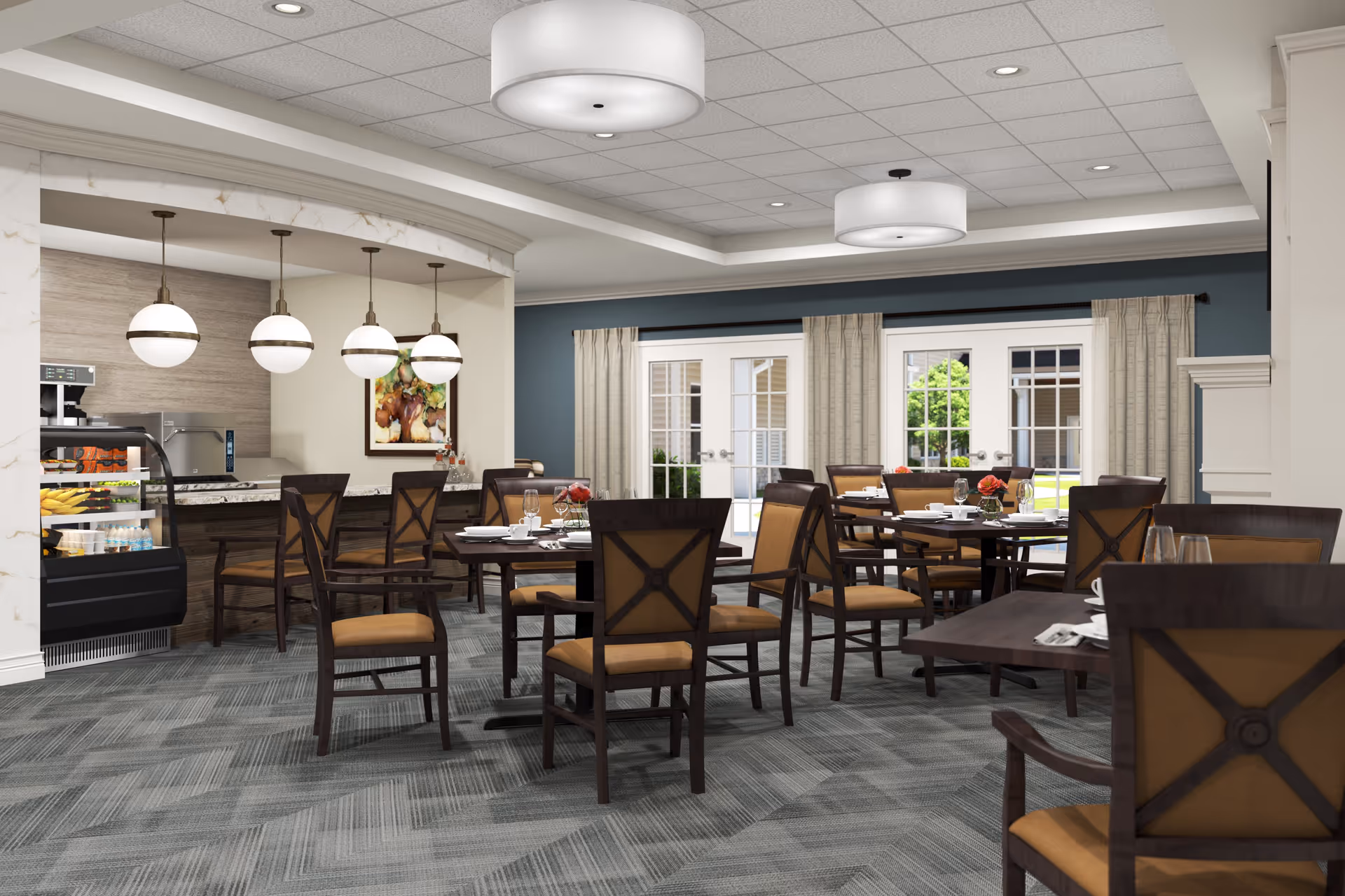 A dining room in a senior living facility with multiple wooden tables and chairs arranged neatly. The tables are set with plates, glasses, and napkins. There are large windows with curtains allowing natural light to enter. A counter area with hanging globe pendant lights and a display case with food items is visible in the background.