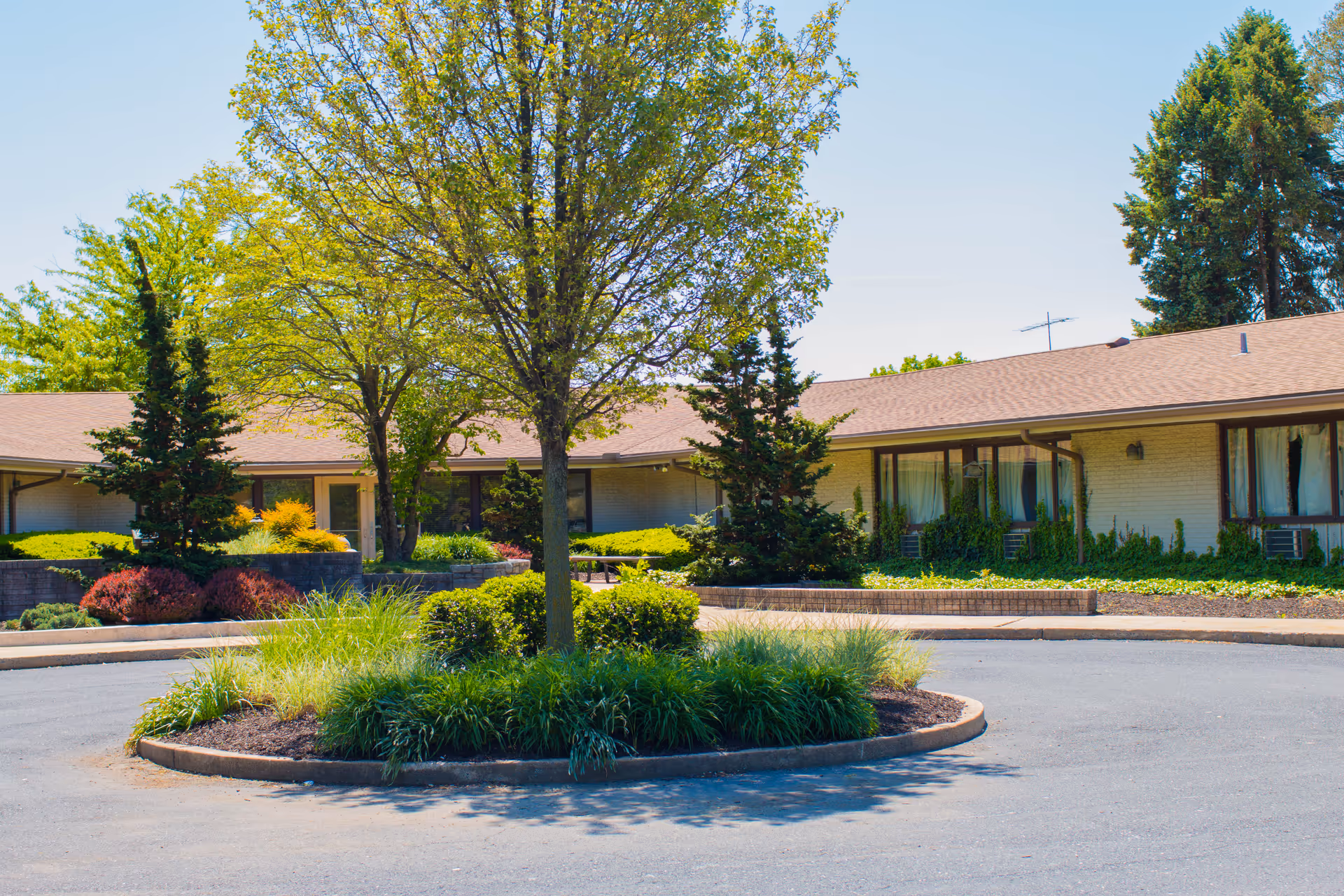 One-story brick senior living building with a circular driveway and a landscaped island of trees and shrubs in front.