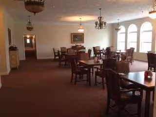 Dining room in a senior living facility with wooden tables and arched windows.