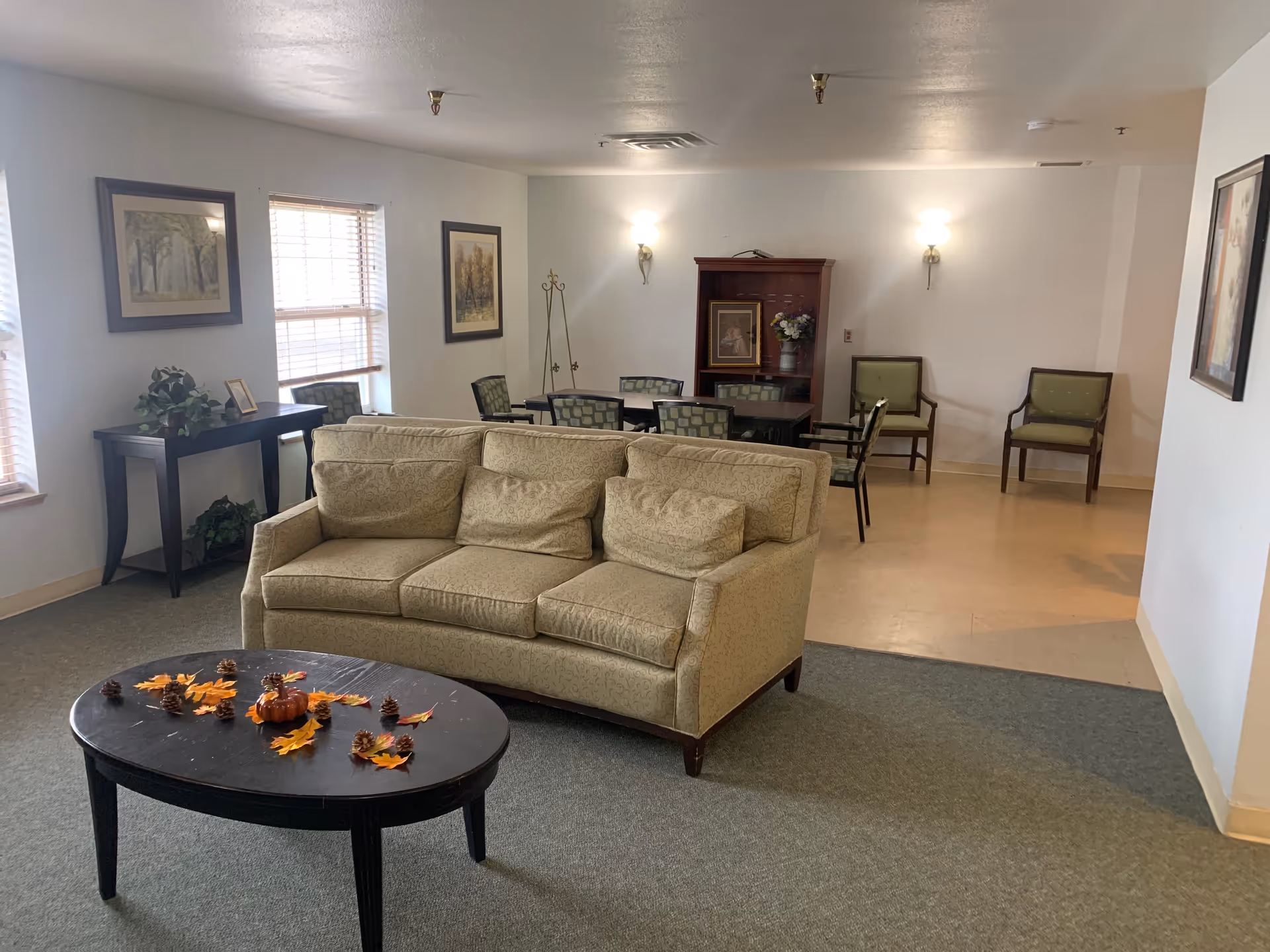 Community lounge with a beige sofa and coffee table with autumn decorations, and a dining table with chairs in the background.