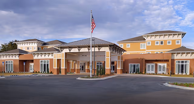 Exterior front view of Summer Vista Assisted Living facility showing a large building with a covered entrance, multiple windows, and an American flag on a flagpole in front.