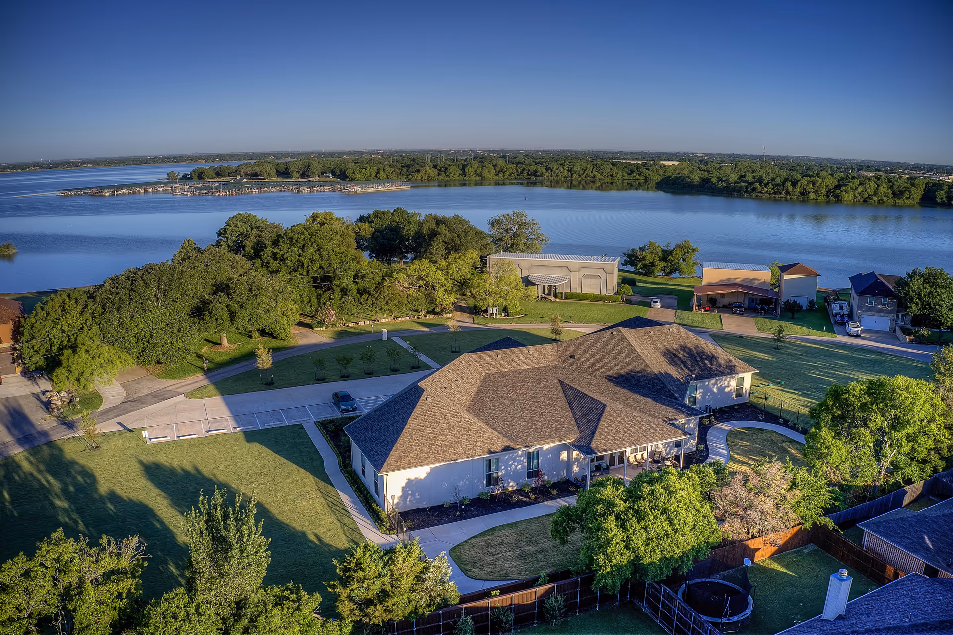 Aerial view of Oakview Assisted Living & Memory Care facility surrounded by green trees and lawns, located near a large body of water with a clear blue sky overhead.