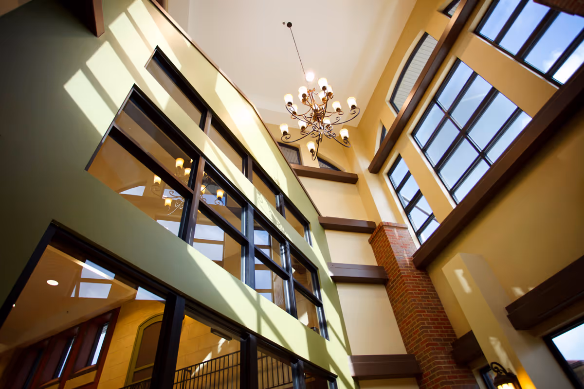 Bright multi-story interior atrium with tall windows, a chandelier, exposed brick column and balconies overlooking the space.