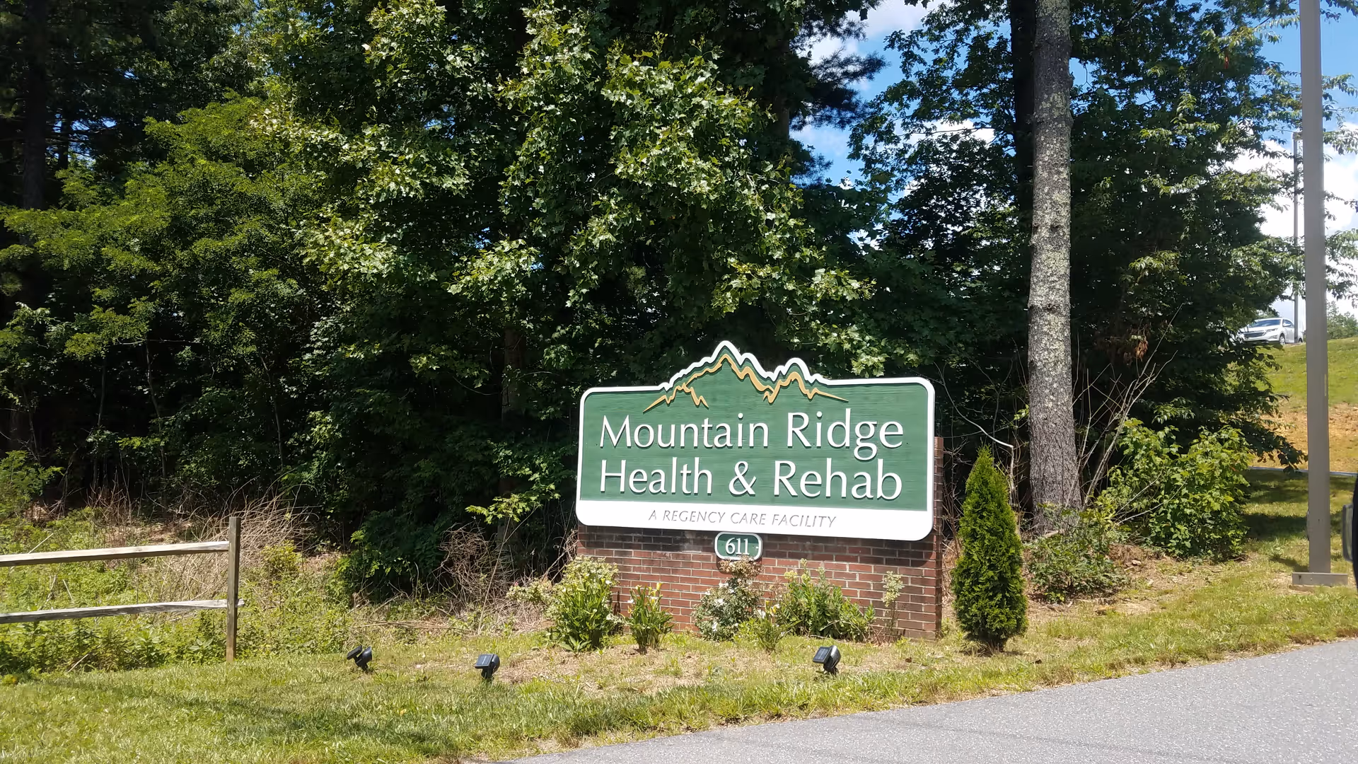 Green sign reading Mountain Ridge Health & Rehab mounted on brick base beside trees.