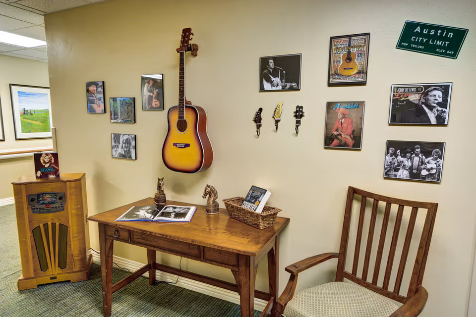 A cozy interior seating nook with a wooden table, chair, wall-mounted guitar and framed photos on the wall.