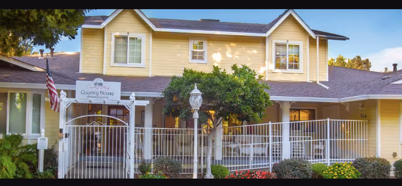 Yellow two-story senior living building with a gated front porch and a sign reading 'Country House'.