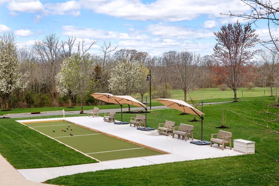 A bocce ball court with seating and umbrellas in a landscaped outdoor area.