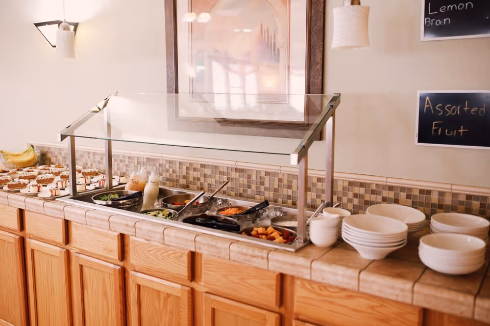 Buffet-style salad bar with bowls, plates, and assorted foods on a tiled counter in a dining area.