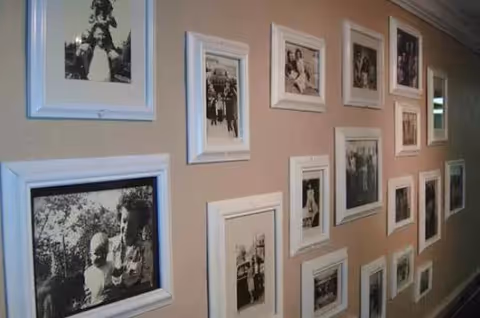 A beige wall decorated with multiple framed black and white photographs arranged in a grid pattern, depicting various people and moments.