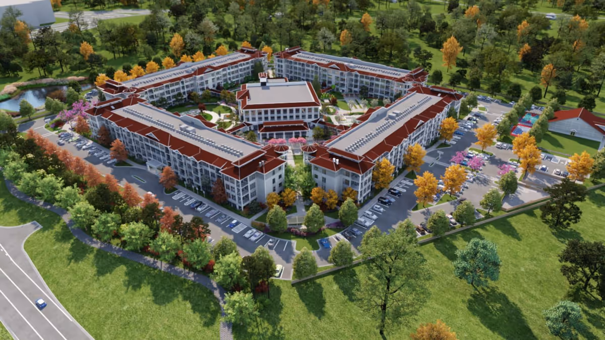 Aerial view of Symphony Park, a luxury independent senior living resort, showing a large, multi-wing building complex with red roofs surrounded by landscaped gardens, trees with autumn foliage, parking lots, and walking paths in a green, park-like setting.