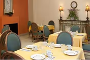 Dining room with yellow tablecloths, place settings, and green upholstered chairs.
