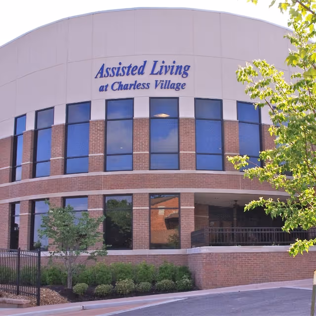 Front exterior of a brick assisted living building with large windows and a sign reading "Assisted Living at Charless Village".