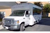 A white passenger shuttle bus parked outside a building, with text on the side indicating it is associated with David Jones Church of Christ.
