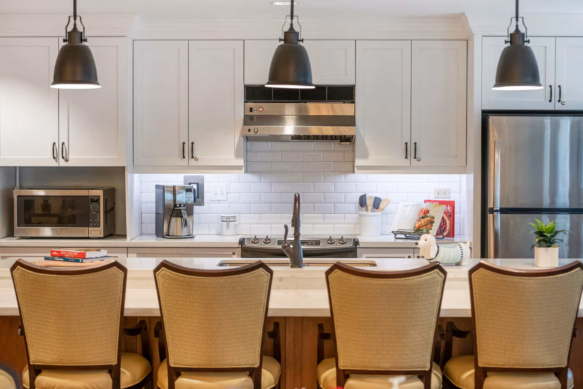 Bright modern kitchen with white cabinets, stainless steel appliances, pendant lights, and an island with four bar stools.