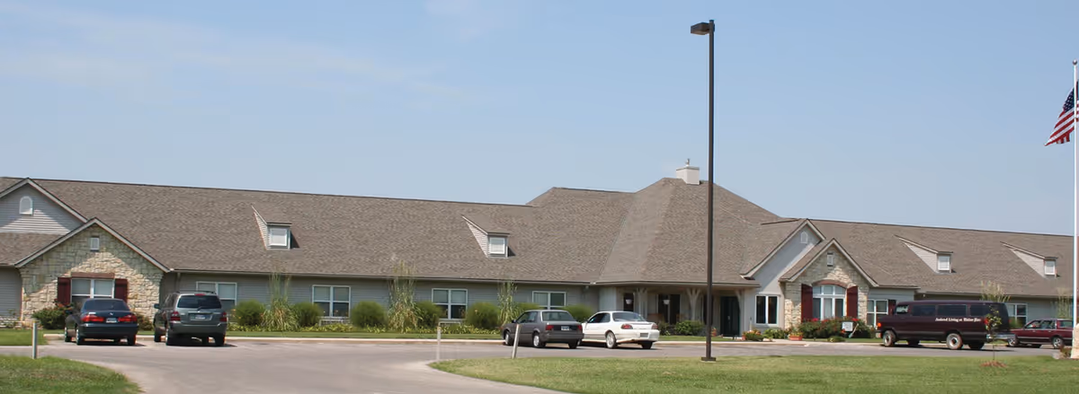 Exterior front of Windsor Place Coffeyville, a brick senior living building with parked cars and flag.