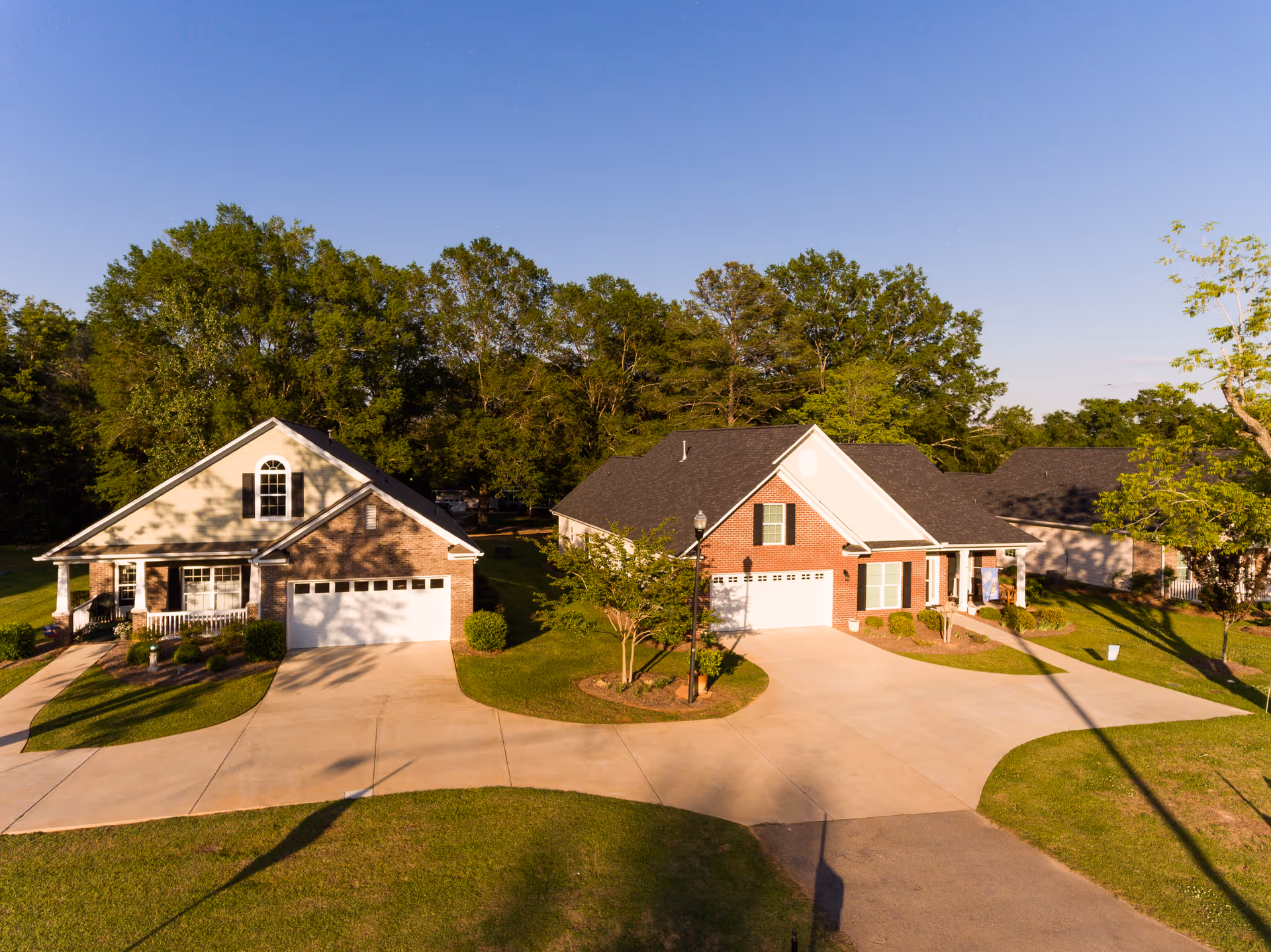 Two single-story residential buildings with garages, surrounded by green lawns and trees under a clear blue sky.