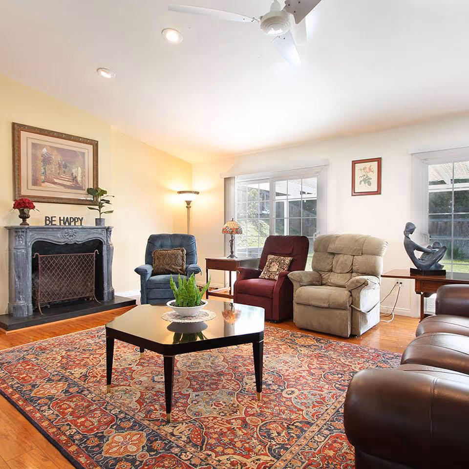 Bright living room with a patterned area rug, central coffee table, several recliners and a fireplace.
