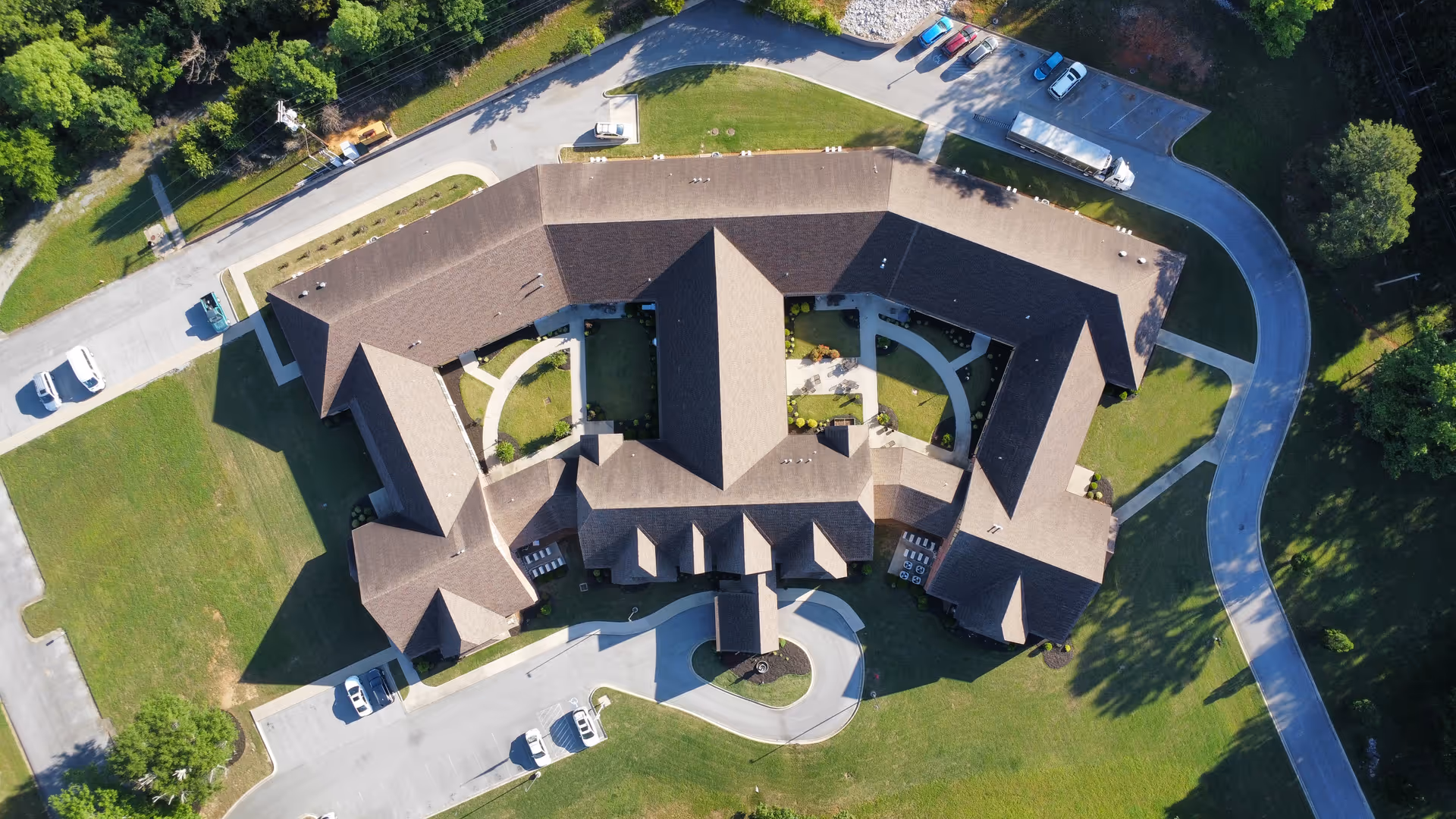Aerial view of Woodcrest Assisted Living showing the building with a central courtyard, surrounding driveways, parking areas, and lawns.