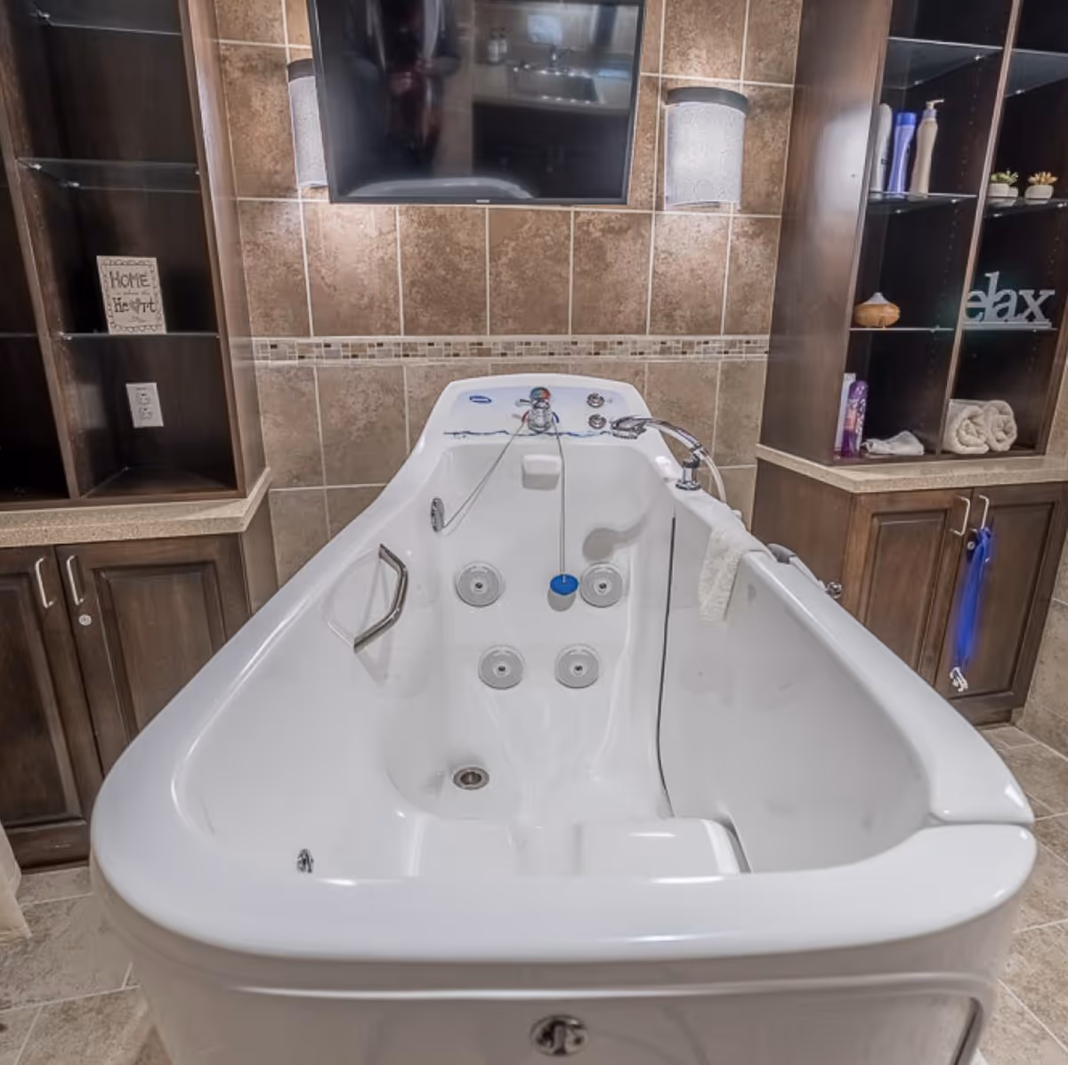 A white walk-in bathtub with jets and grab handles set in a tiled bathroom flanked by wooden cabinets and shelving.