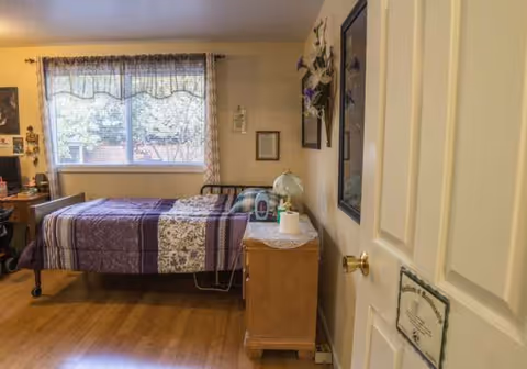 Cozy senior living bedroom with a quilted bed, nightstand, lamp, and window.