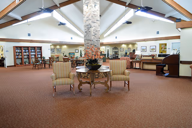 Spacious senior living common lounge with seating, a round table and decorative central brick column under a vaulted ceiling.