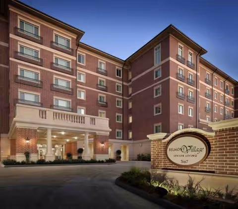 Red brick senior living building with covered entrance and Belmont Village sign at twilight.