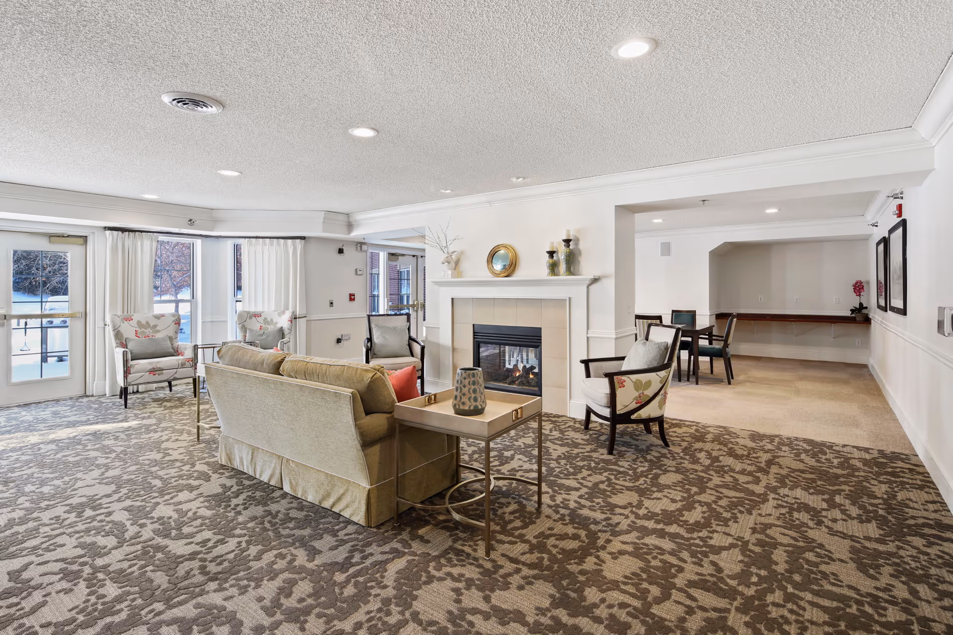Communal living room with sofas and chairs arranged around a central fireplace and large windows.
