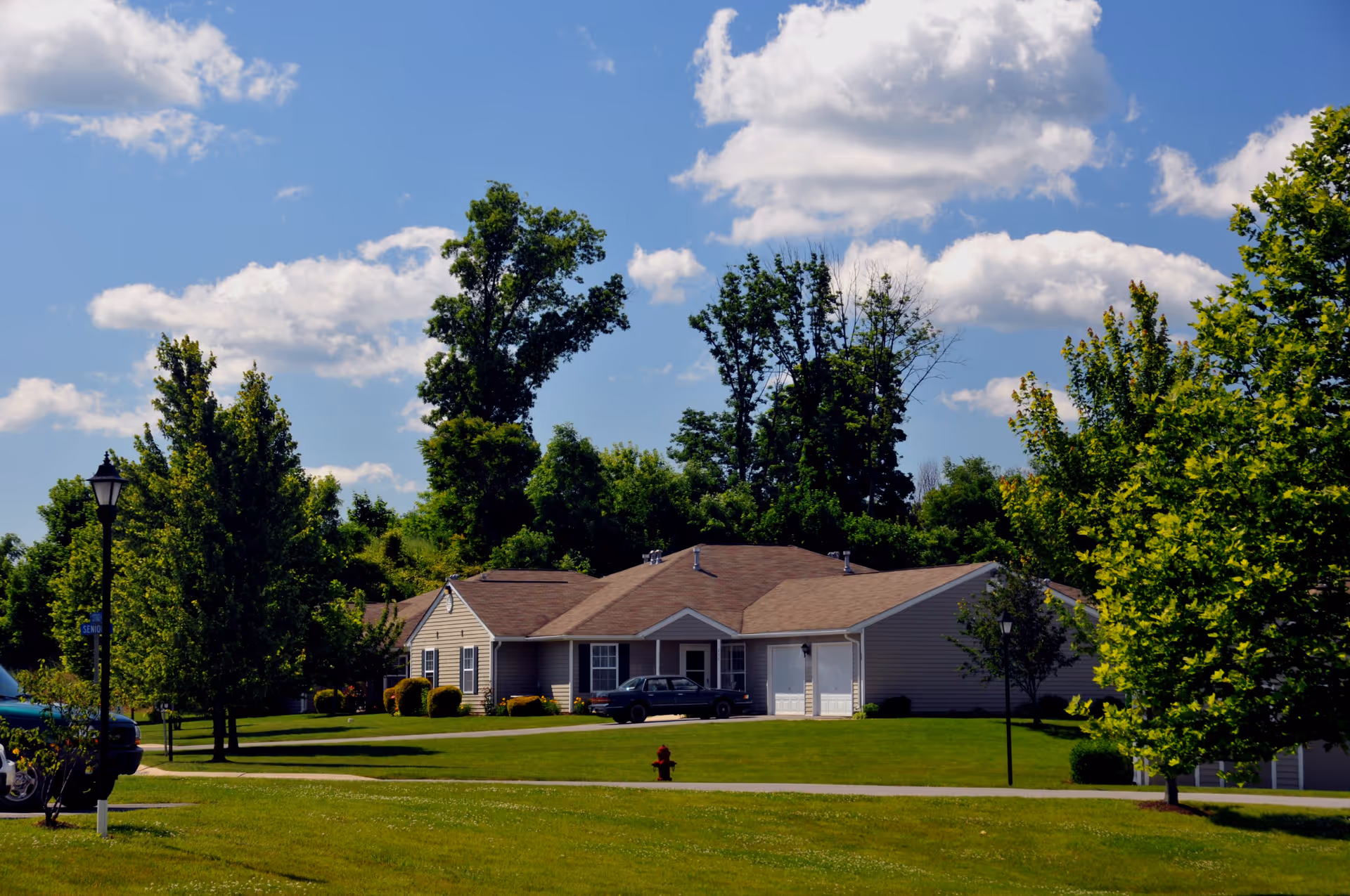 Single-story cottage-style homes with garages on a manicured lawn under a blue sky.