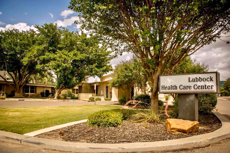 Front entrance of Lubbock Health Care Center with a sign, trees, and landscaped circular driveway.
