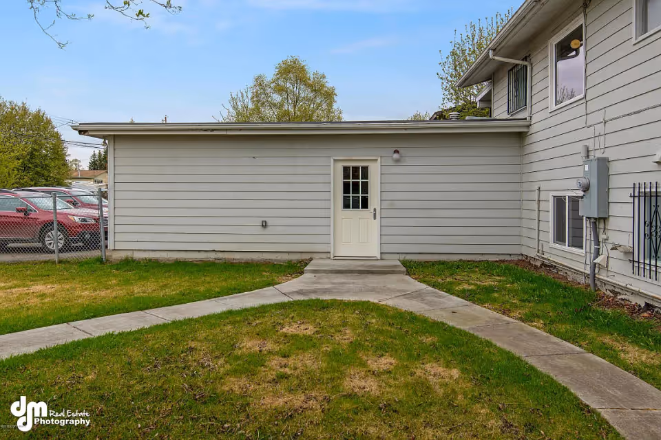 White-sided building exterior with a centered door, curved concrete walkway and a grassy yard in front.