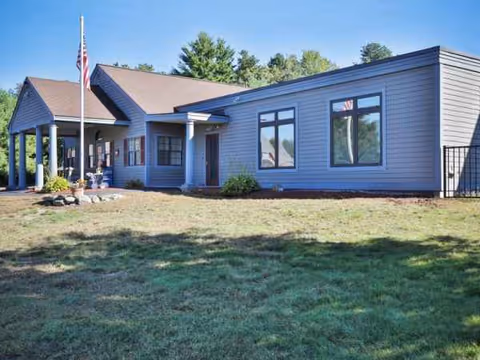 A single-story Merrimack Meadows facility exterior with flagpole, windows, and a front entrance.