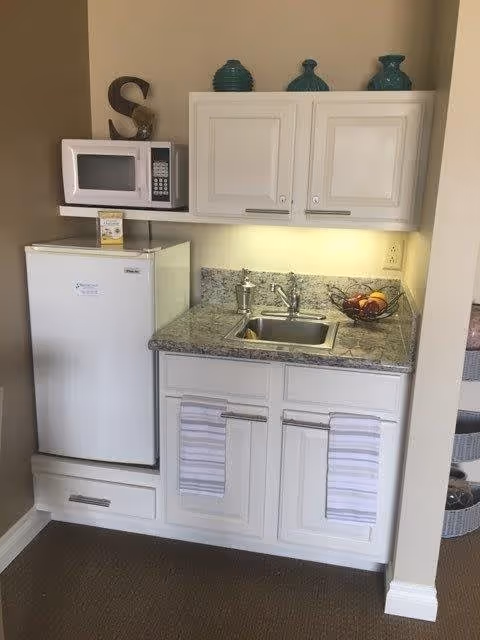 Small kitchenette with a mini fridge, microwave, sink, granite countertop and white cabinets.