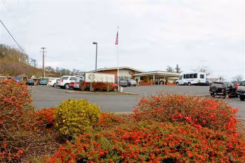 Exterior view of Rose Haven Nursing Center with entrance, flag, cars, and landscaping.