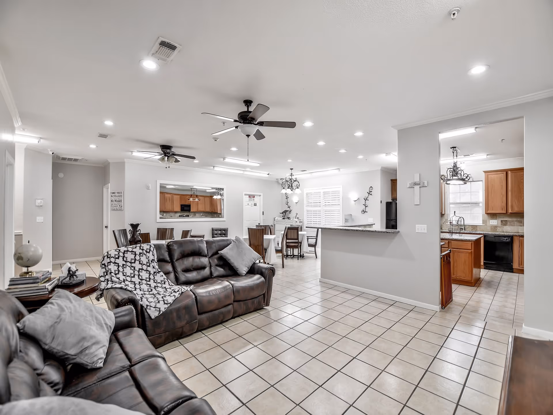 Open-concept living area with leather sofas and tiled floor looking toward a dining area and kitchen under ceiling fans.