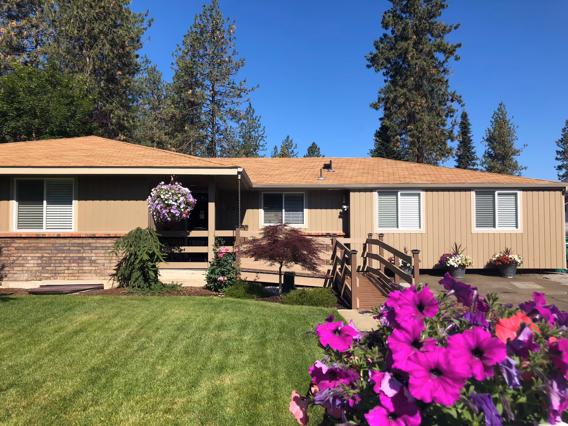 Single-story beige ranch-style home with a front ramp, manicured lawn, and purple flowers in the foreground.