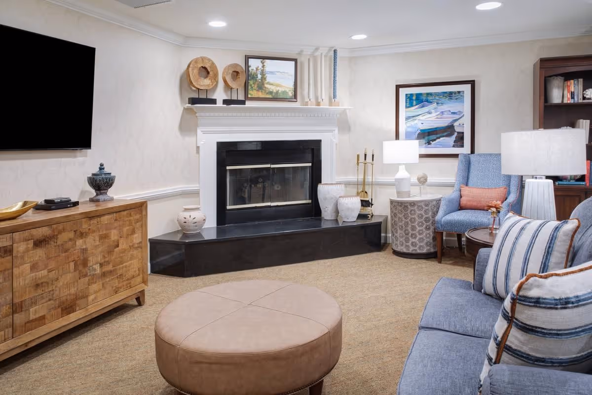 Cozy common-area living room with a fireplace, TV, upholstered seating, ottoman, and decorative accents.