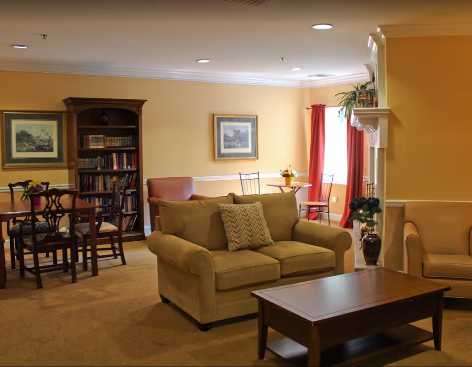 Comfortable common room with sofas, a coffee table, bookcase, dining table and chairs, and a small bistro table by a window.