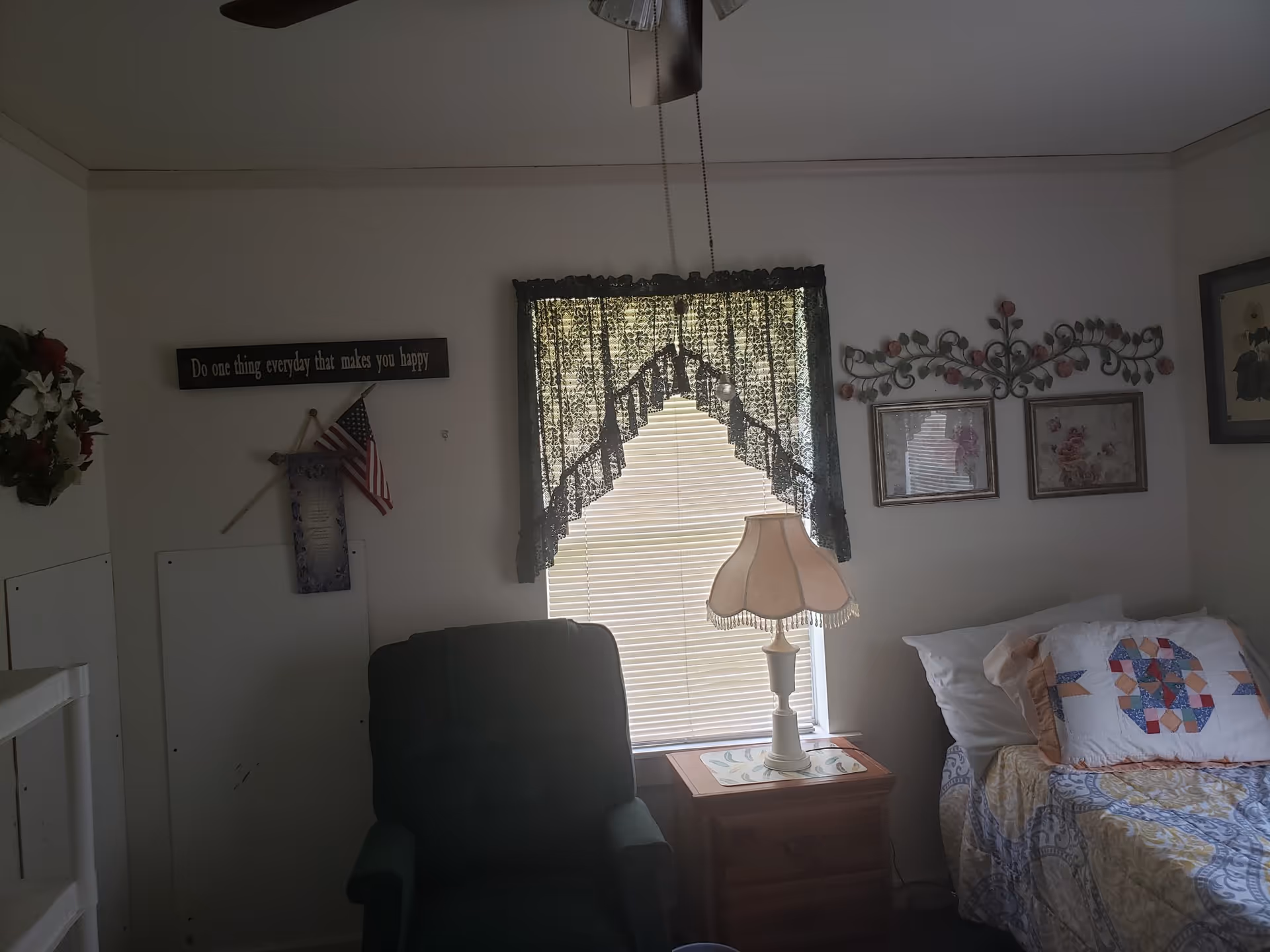 Cozy bedroom in a senior facility with a bed, recliner, window, and wall decor.