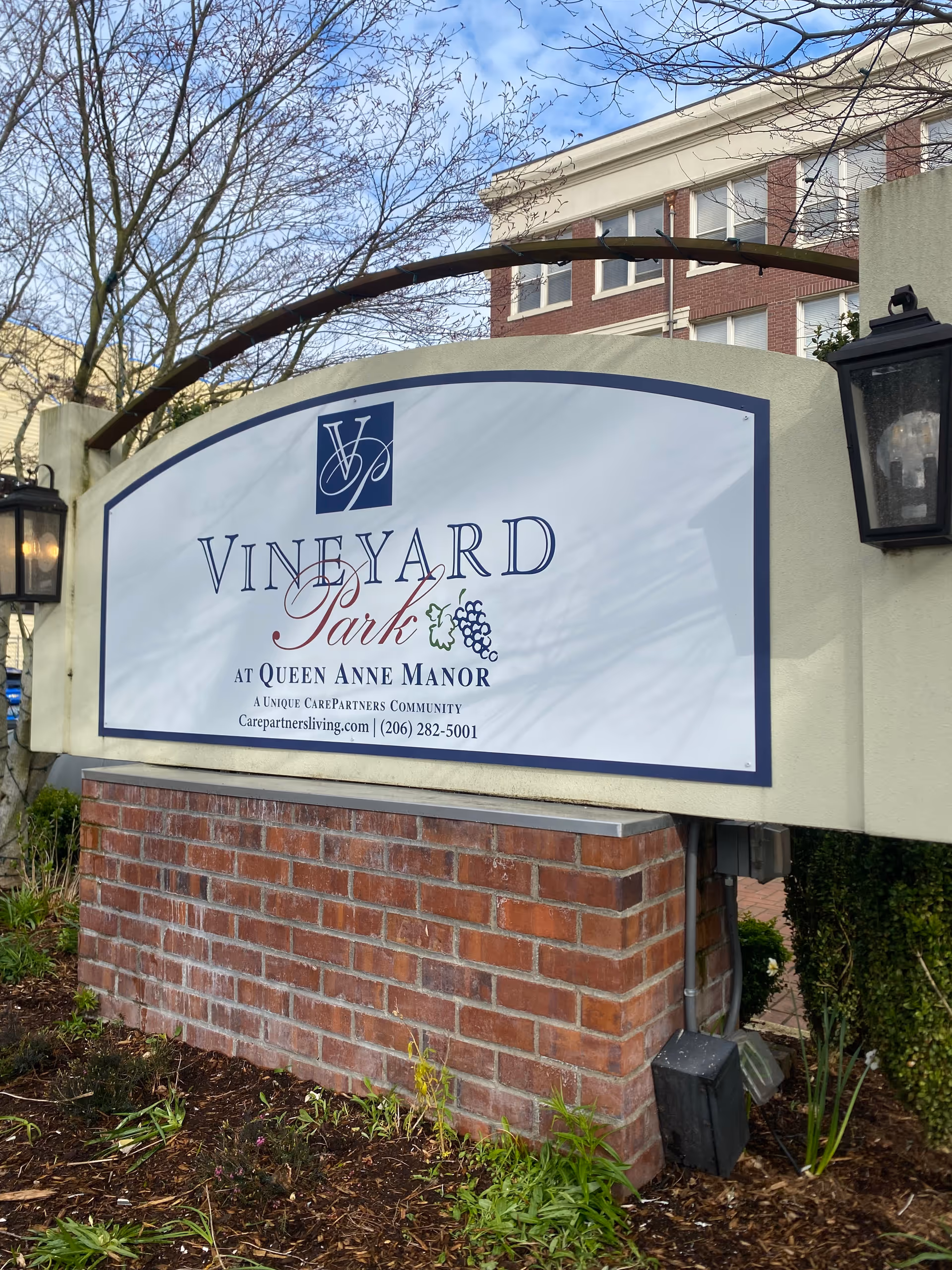 Entrance sign reading "Vineyard Park at Queen Anne Manor" mounted on a brick base in front of the building.